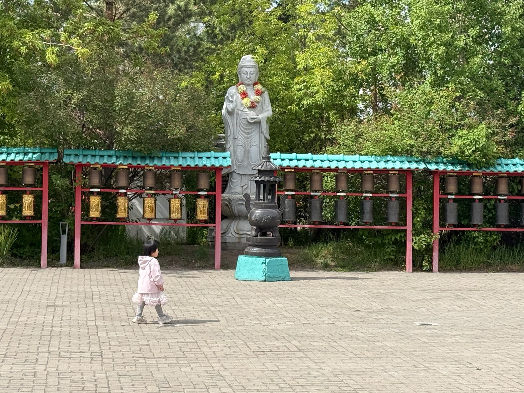 Child walking past a Buddha statue and prayer wheels in a Mongolian temple garden