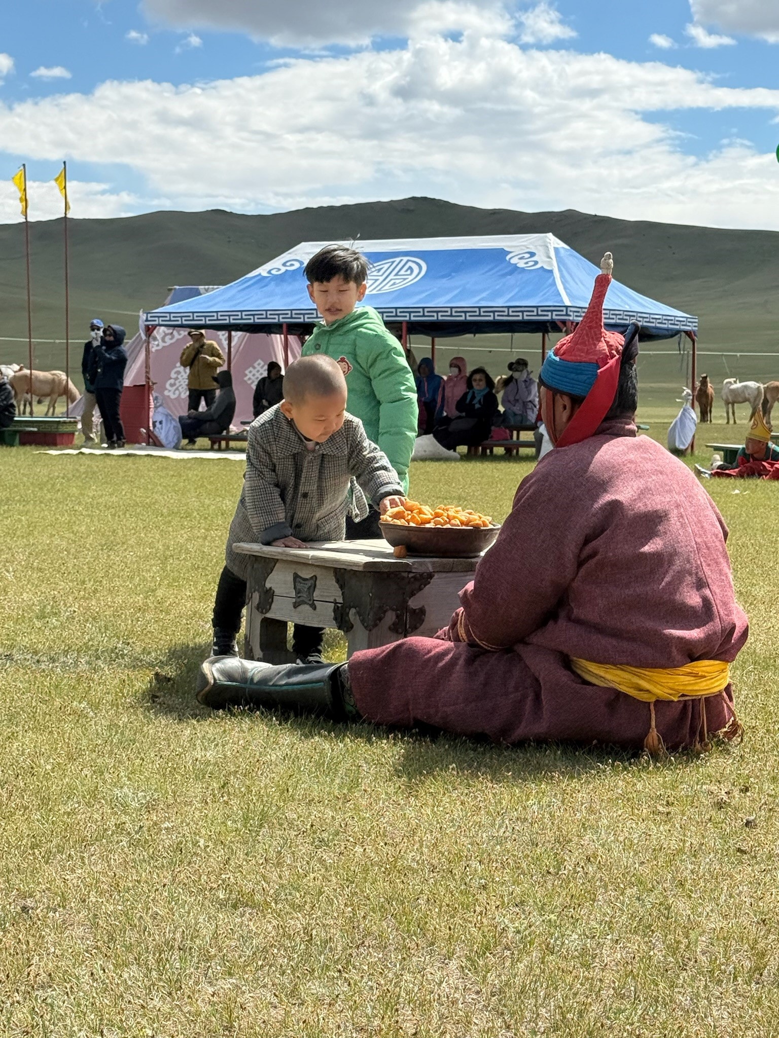 Children and elders gathered at a traditional Mongolian festival table on the steppe